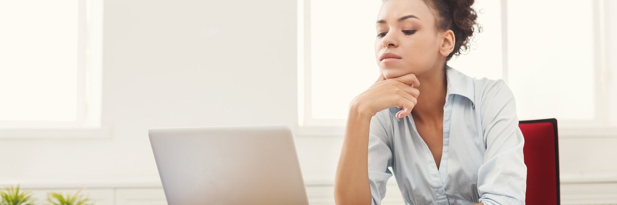 A woman looking at her laptop with papers on her desk.