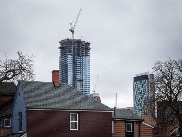 Picture of Cranes building a condominium high rise skyscraper taken in Toronto, with smaller wooden houses and individual buildings are visible in the foreground. Toronto is the most populous city in Canada, the provincial capital of Ontario, and the cent