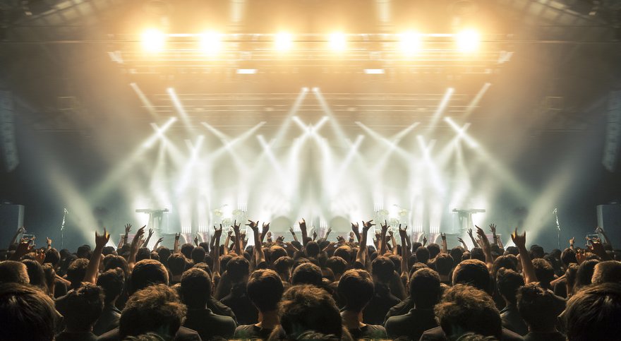 A crowd with hands in the air backlit by stage lights at a concert.